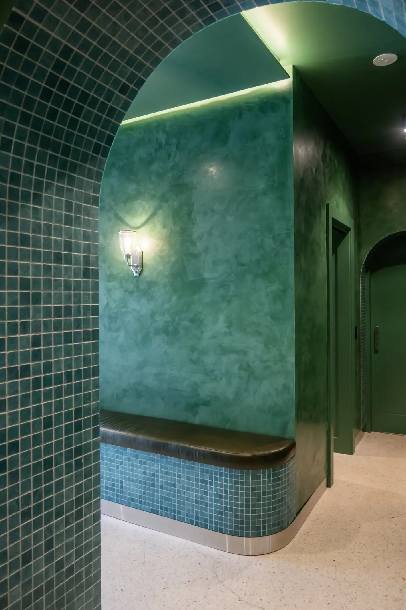 Green mosaic tiled arch corridor with wall sconce lighting and curved bench seat at The Skin Bar Manly Sydney