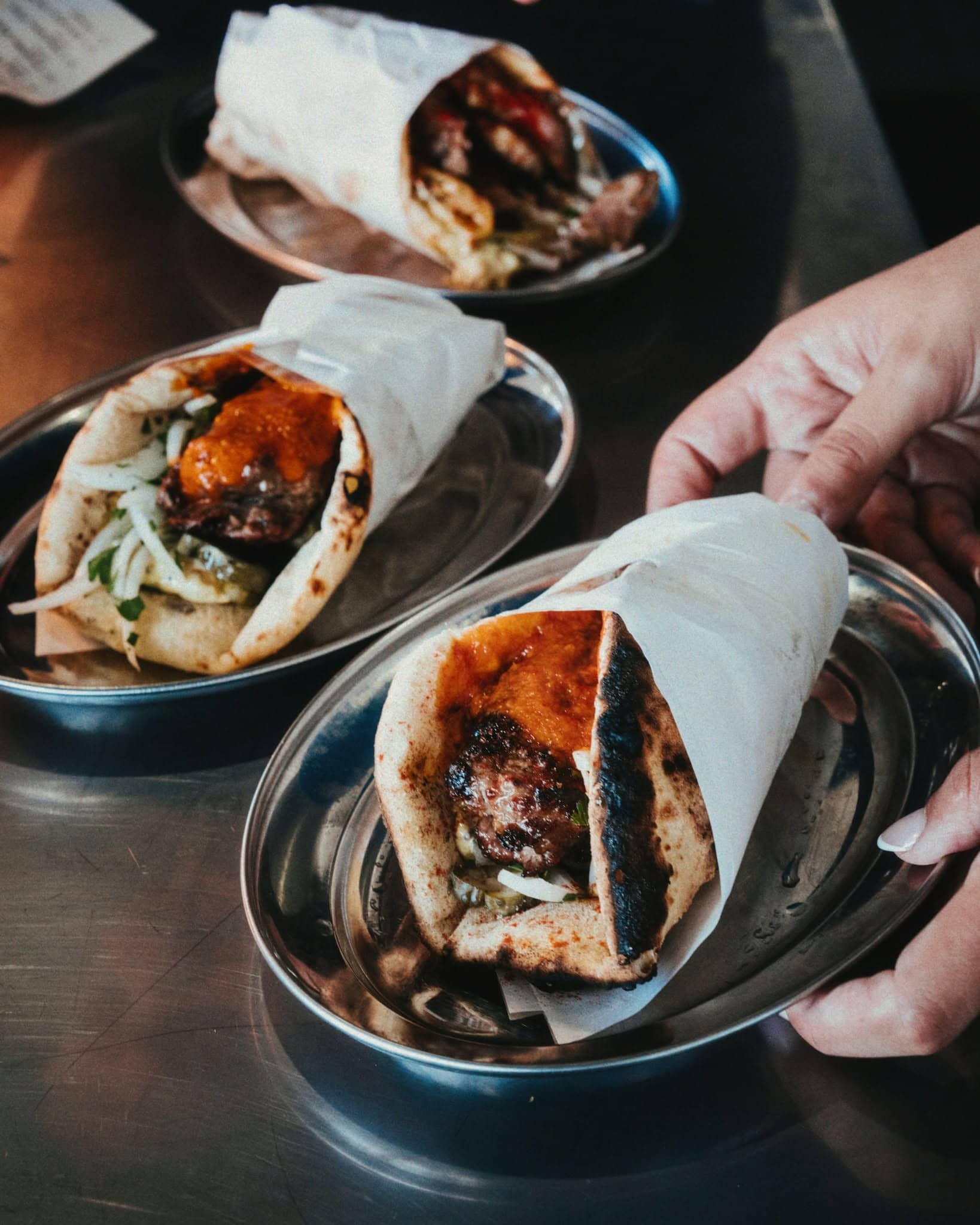 A selection of greek gyros wrapped in paper and sitting atop silver trays at Olympic Meats in Marrickville.