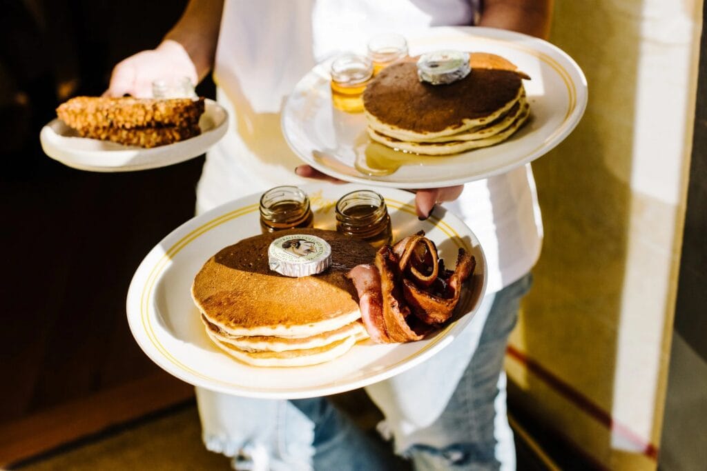 Server holding pancake stacks with bacon and maple syrup jars at Happyfield Sydney