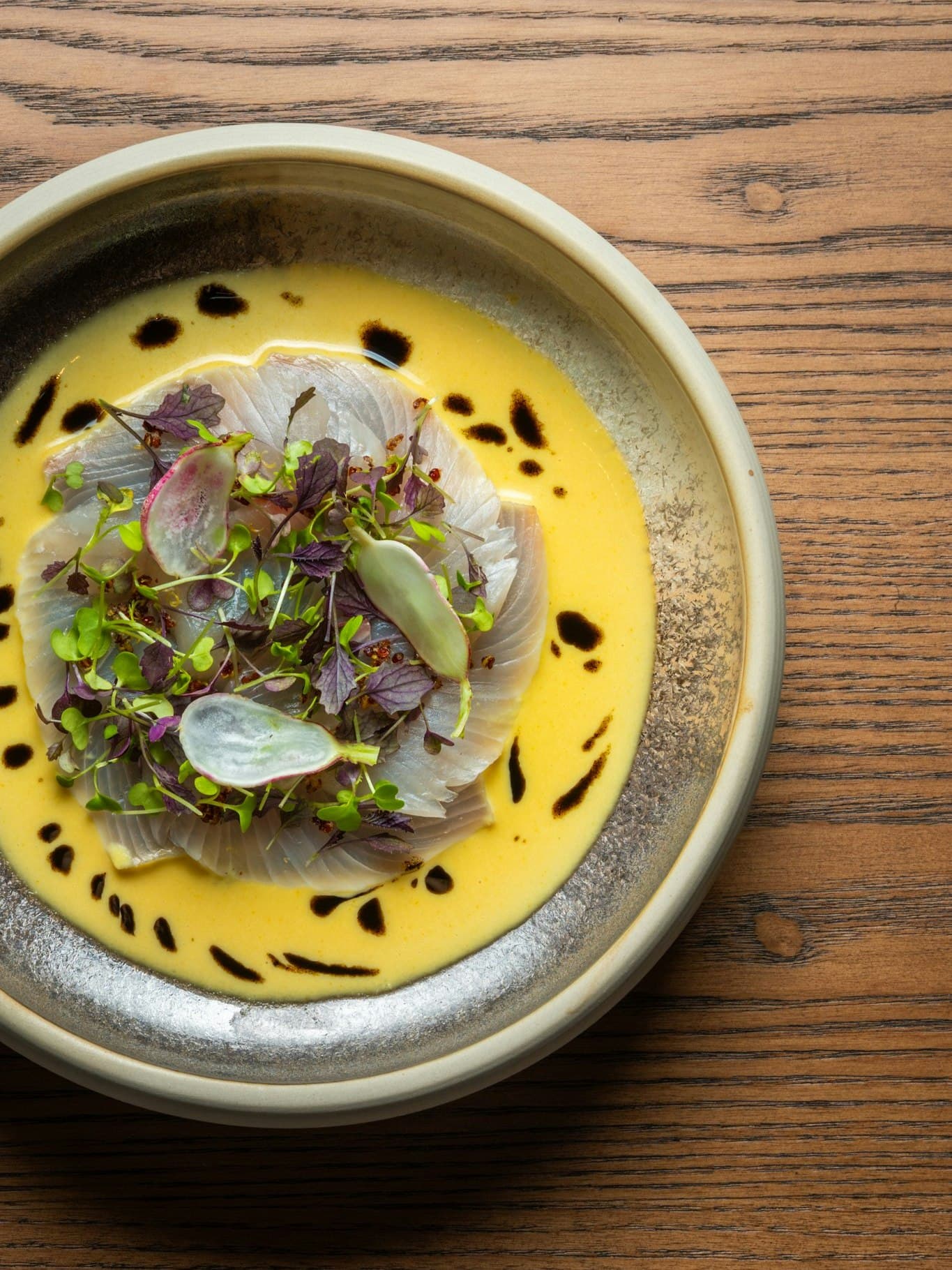 A bowl of sashimi in a bath of yellow sauce, dotted with soy sauce at AORI in sydney.