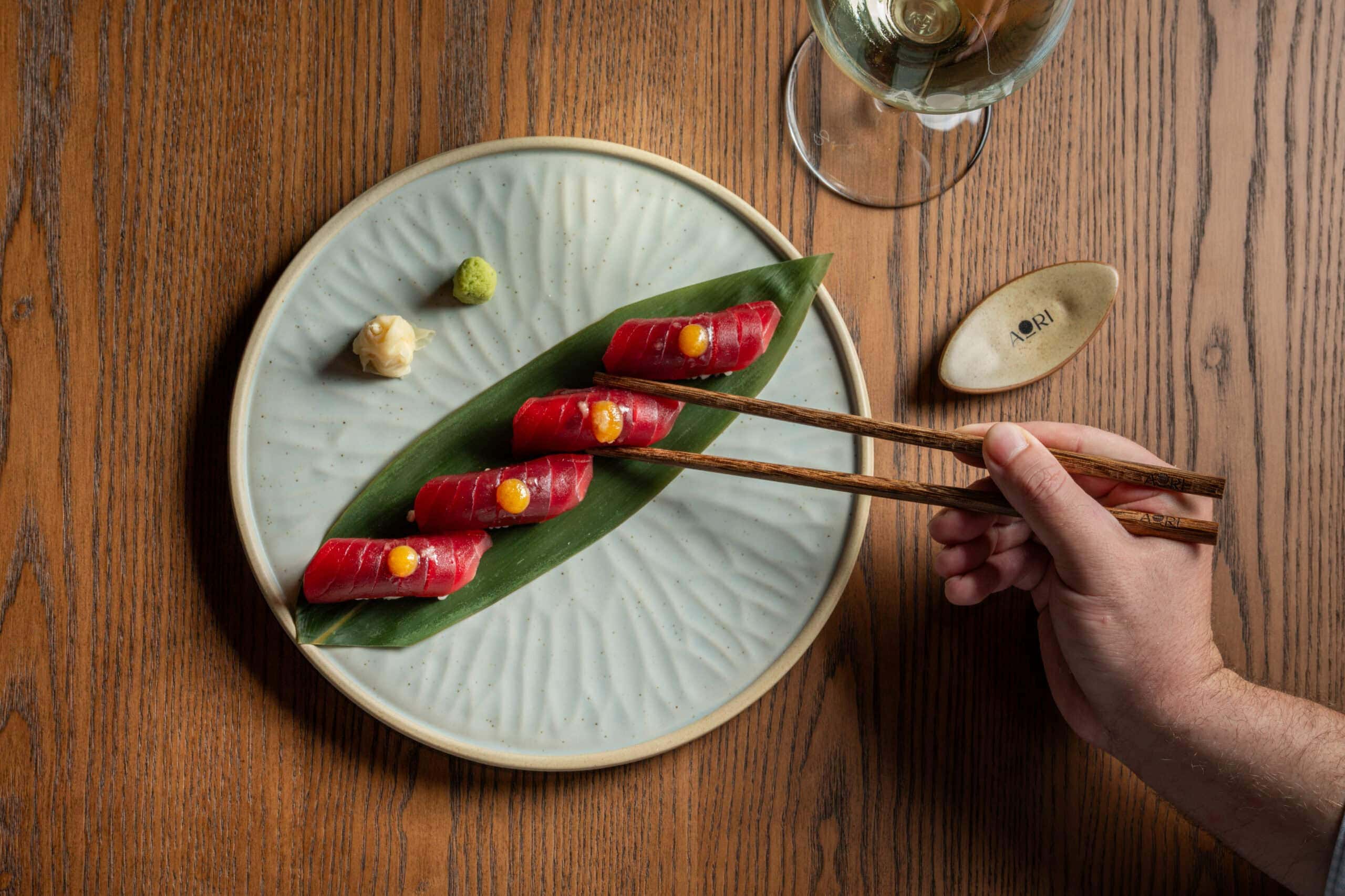 Someone using chopsticks to pick up a delicate piece of nigri from atop a banana leaf at AORI in sydney.