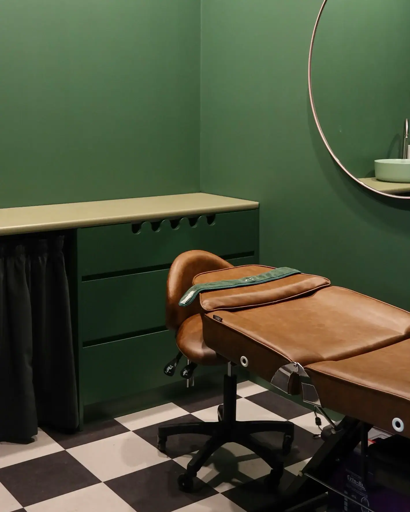 Green-walled facial treatment room with leather bed saddle stool and checkered floor at The Skin Bar Manly Sydney