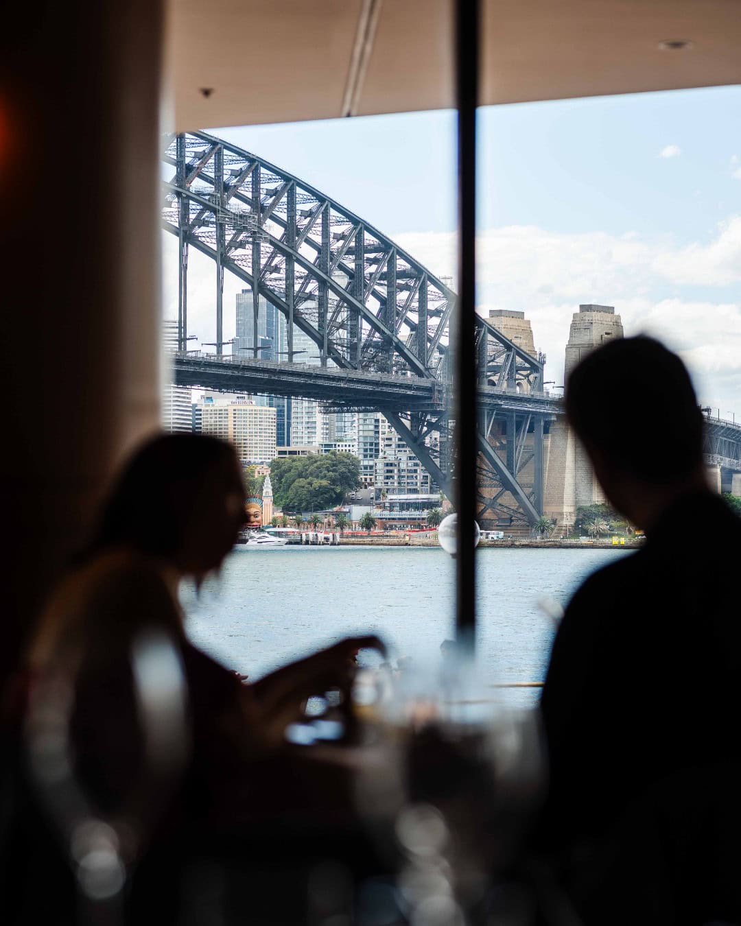Two silhouettes in the window of fine dining restaurant Aria in Sydney, with the harbour bridge in the background.