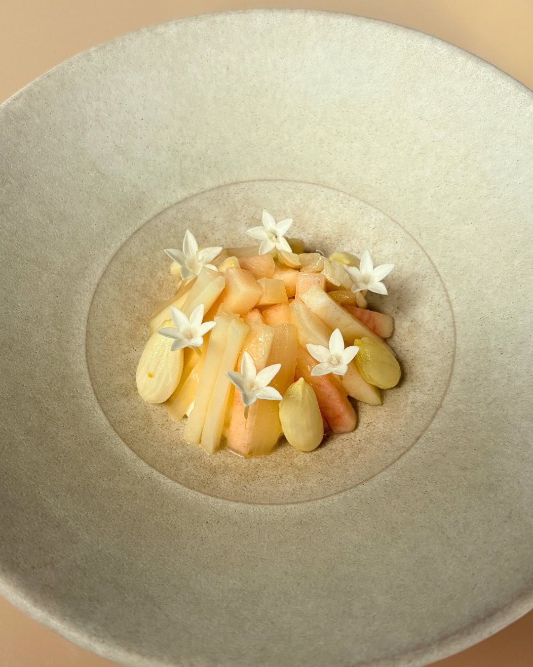 A close up of a white asparagus dish on a large plate, dressed with white edible flowers at bennelong in circular quay.