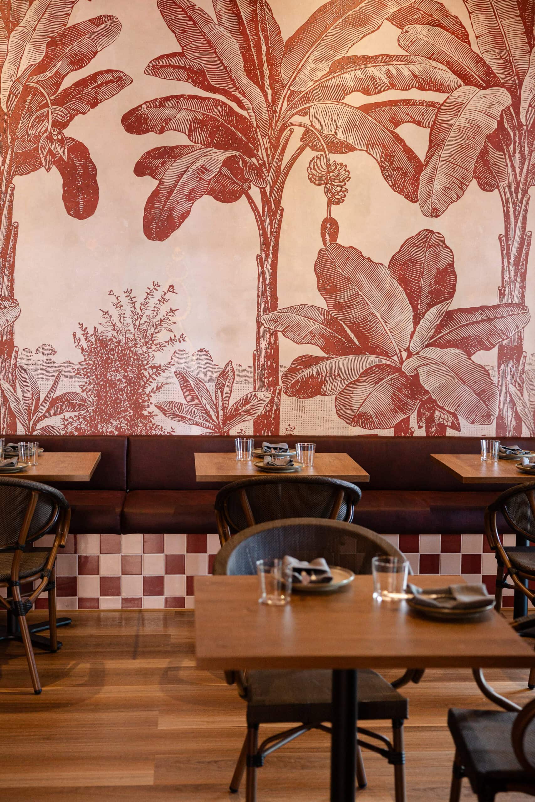 Banquette seating at Picoso Mexican Bar Y Cocina, Adelaide, set against a large terracotta tropical mural featuring banana trees, with checkered tile detail below.
