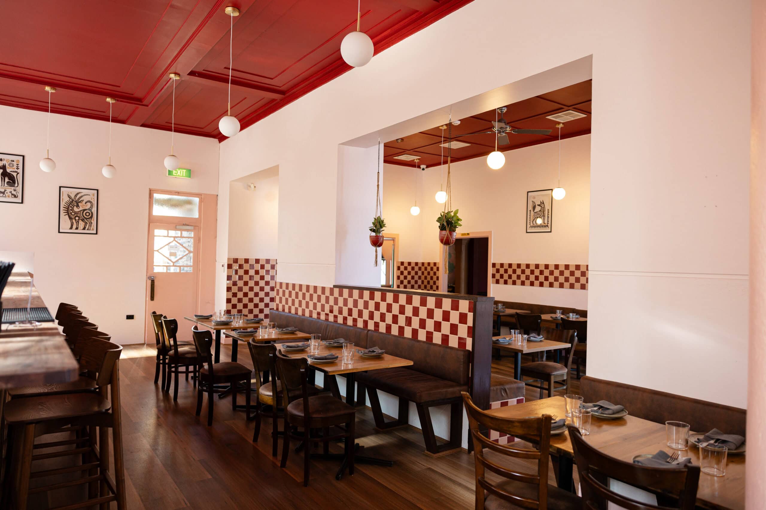 Interior dining room at Picoso Mexican Bar Y Cocina, Adelaide, with a red coffered ceiling, red-and-white checkered tile wainscoting, leather banquette seating, and hanging globe lights.