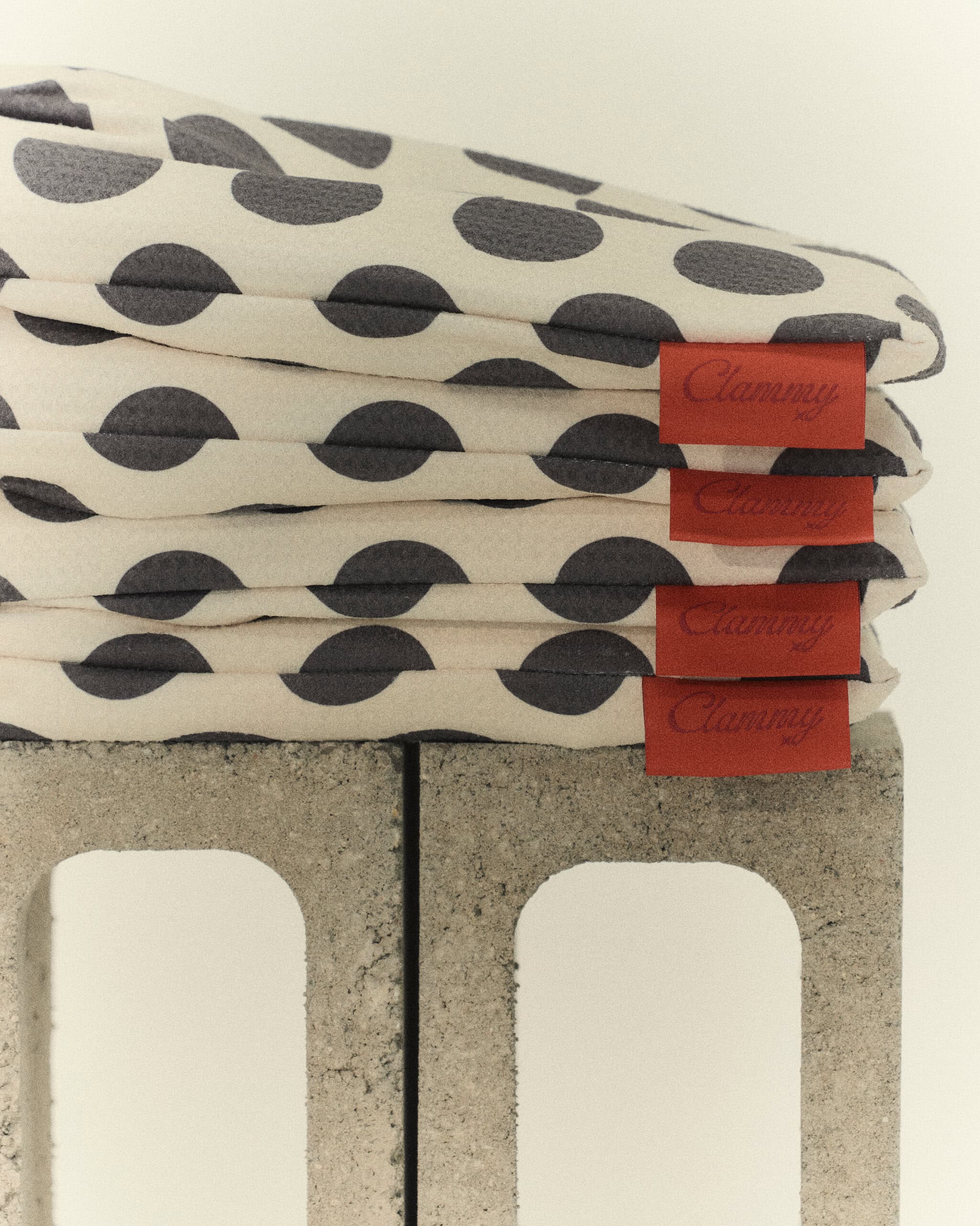 Stack of folded Clammy polka dot waffle-weave towels with red Clammy branded labels on concrete block