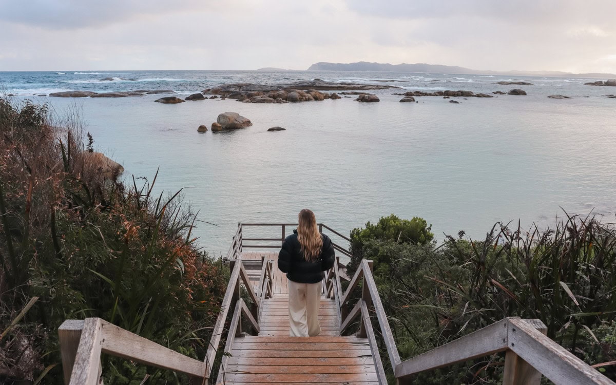 Woman standing on wooden coastal stairs overlooking rocky ocean bay