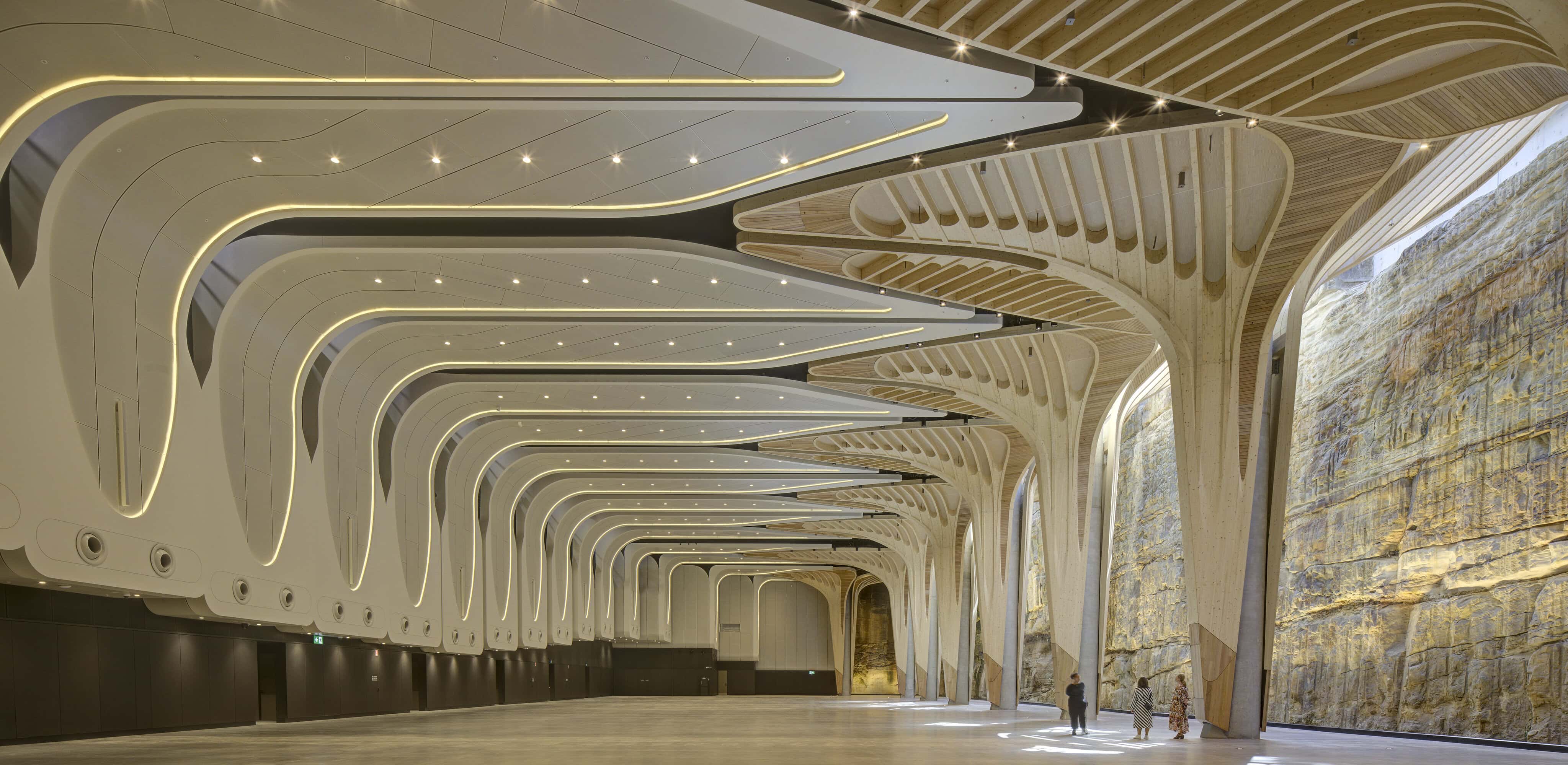 Interior of The Cutaway underground cultural venue with curved timber ribbed ceiling exposed sandstone rock wall and vast open floor at Barangaroo Sydney