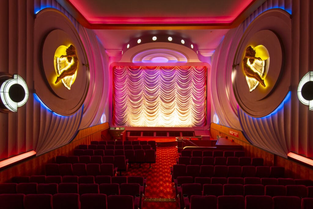 Art Deco auditorium interior with velvet seats illuminated stage curtain and gold wall sculptures at Hayden Orpheum Picture Palace Cremorne Sydney