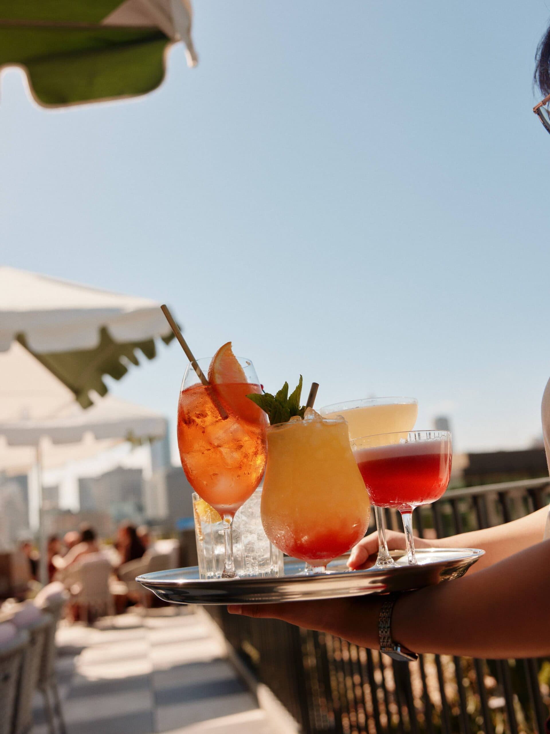 Server carrying tray of cocktails including spritz paloma and coupe on rooftop bar Monica's Paddington Sydney