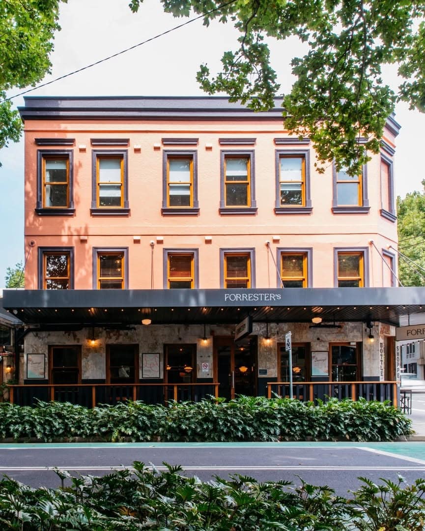 The peach and black exterior of forresters pub in surry hills, surrounded by greenery and trees.