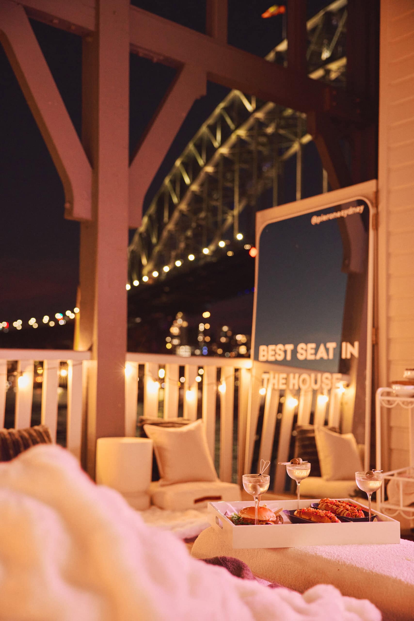 Harbourside Cinema suite balcony with cocktails burgers fairy lights and illuminated Sydney Harbour Bridge at night at Pier One Walsh Bay Sydney