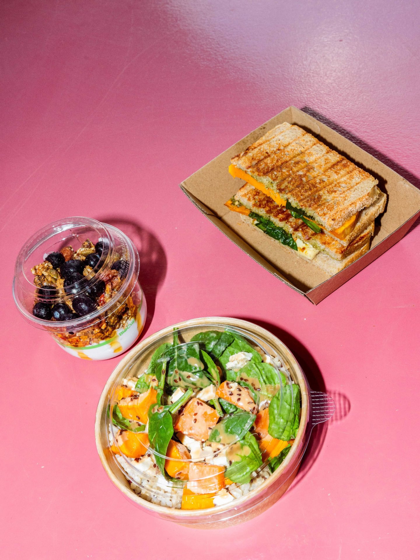 Toastie, salad bowl and yoghurt with granola photographed on a pink table at Kudos by Parla in Launceston.