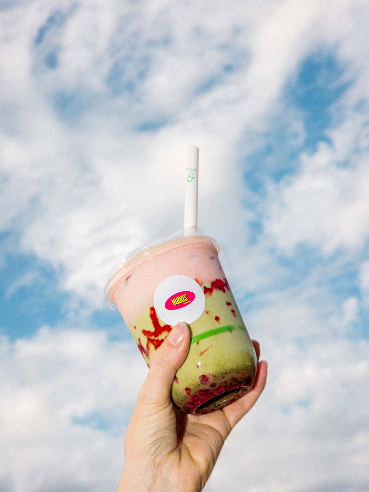 Layered pink and green iced drink from Kudos by Parla held up against a blue sky.