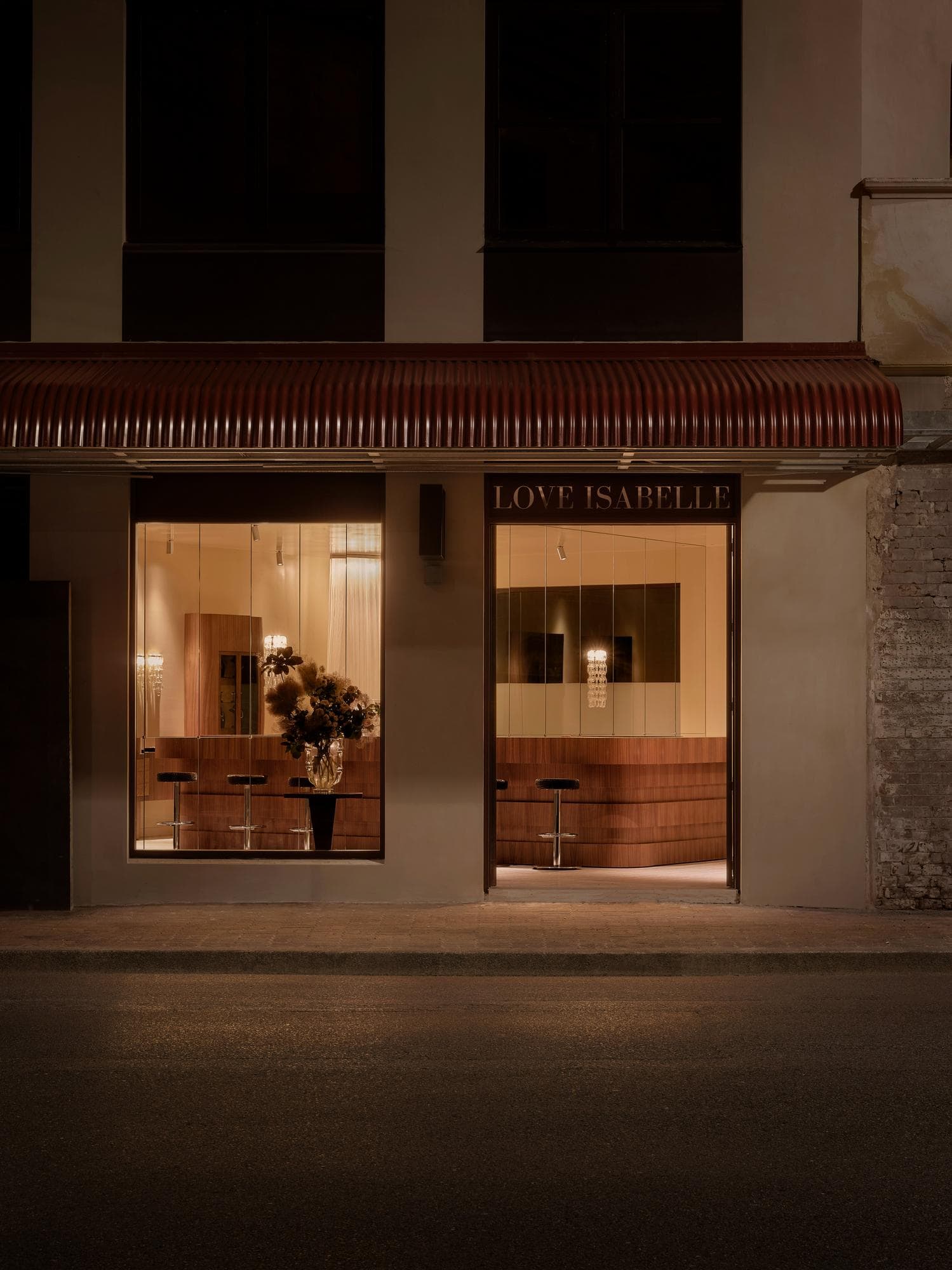 Love Isabelle jewellery store facade at night with terracotta-coloured ribbed awning, illuminated shopfront signage, and warm amber glow emanating through large display windows