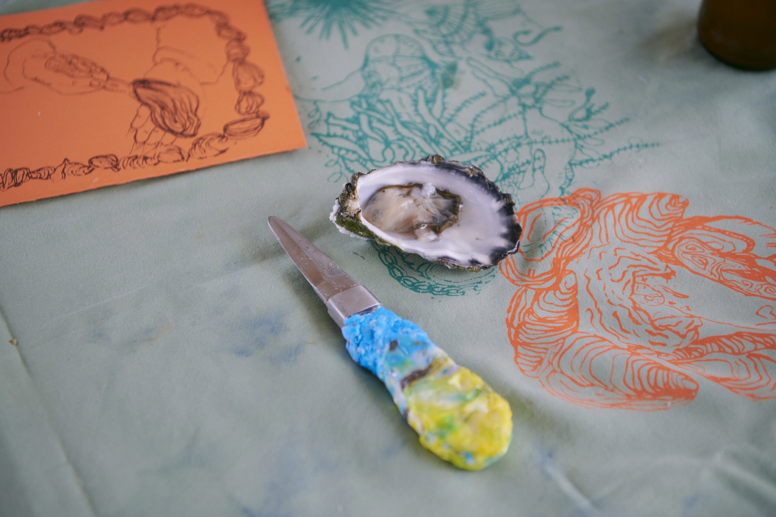 Freshly shucked oyster with hand-painted shucker knife on printed textile at Seascapes oyster shucking workshop Sydney Fish Market Pyrmont