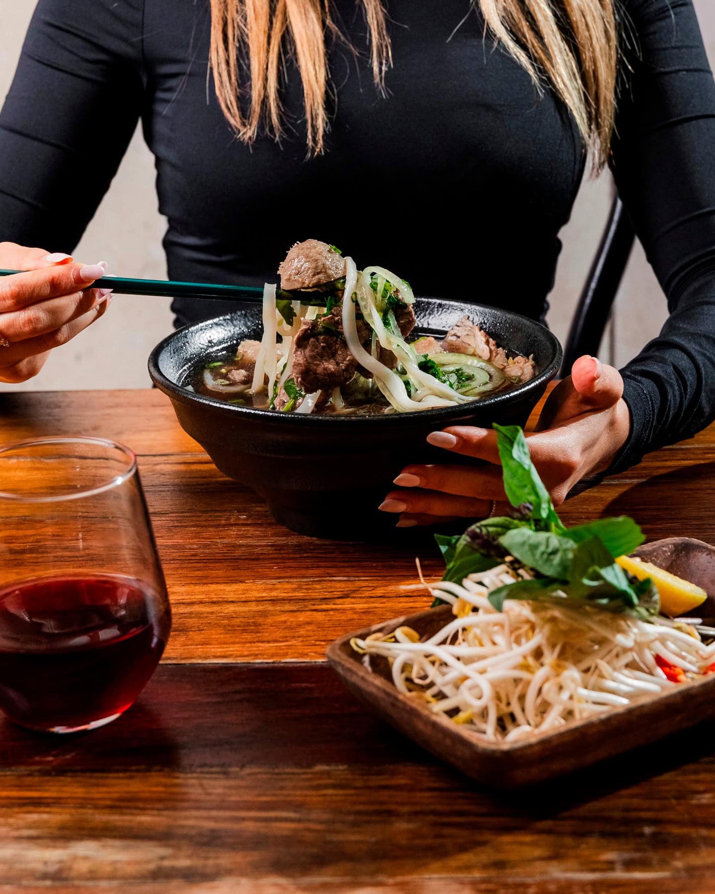 A woman using chopsticks to dig into a bowl of pho at Hello Auntie.