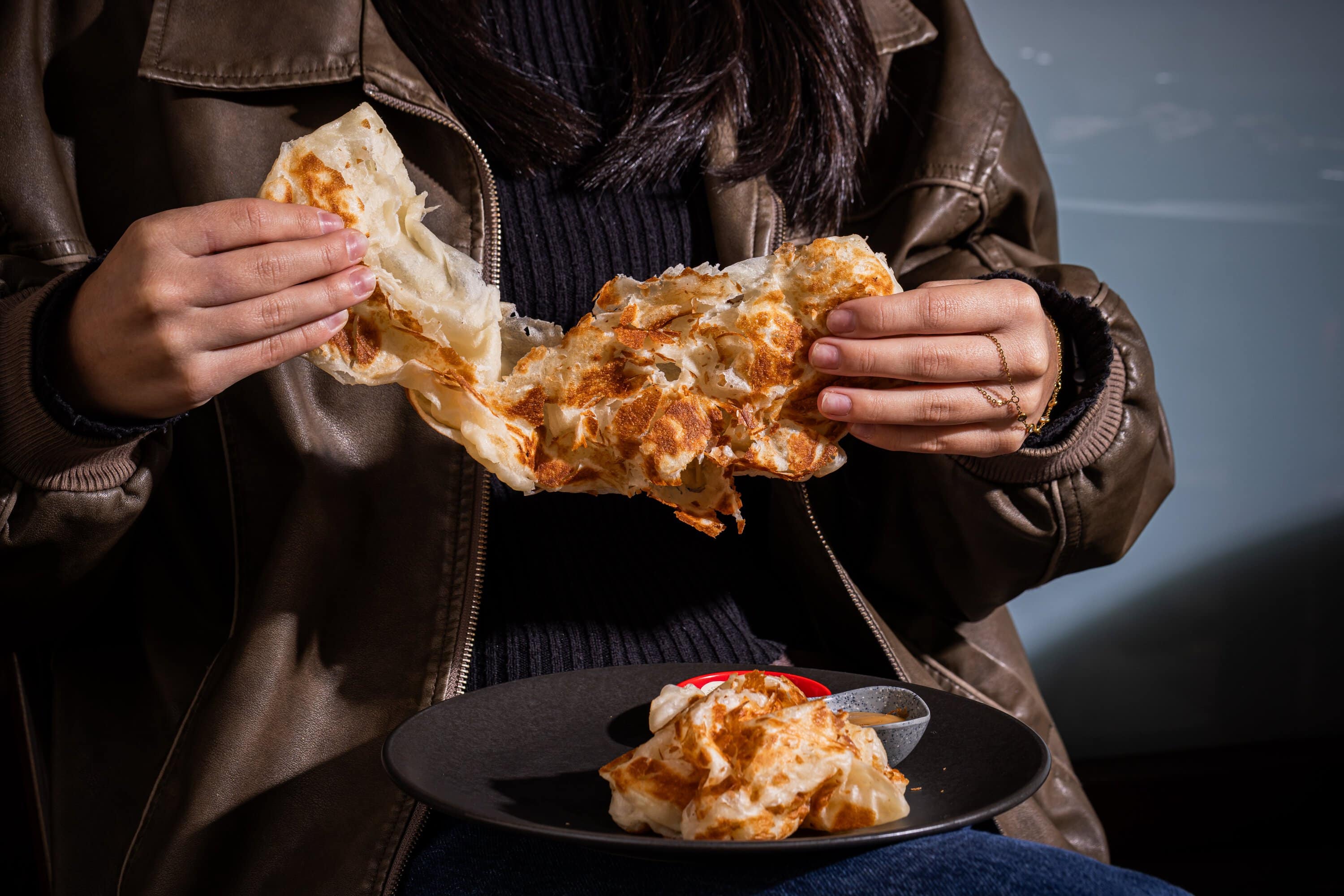 Hands tearing roti canai bread with chicken curry dipping sauce at Kafe Kooks Ultimo Sydney