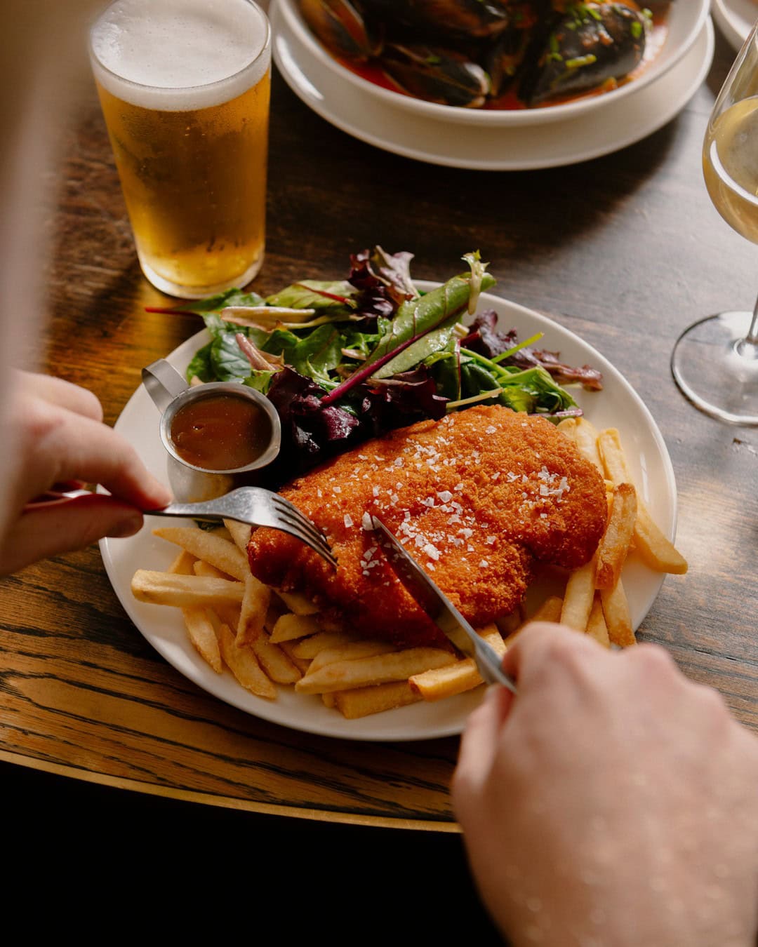 Someone tucking into a plate of chicken schnitzel, salad and chips at the glenmore.