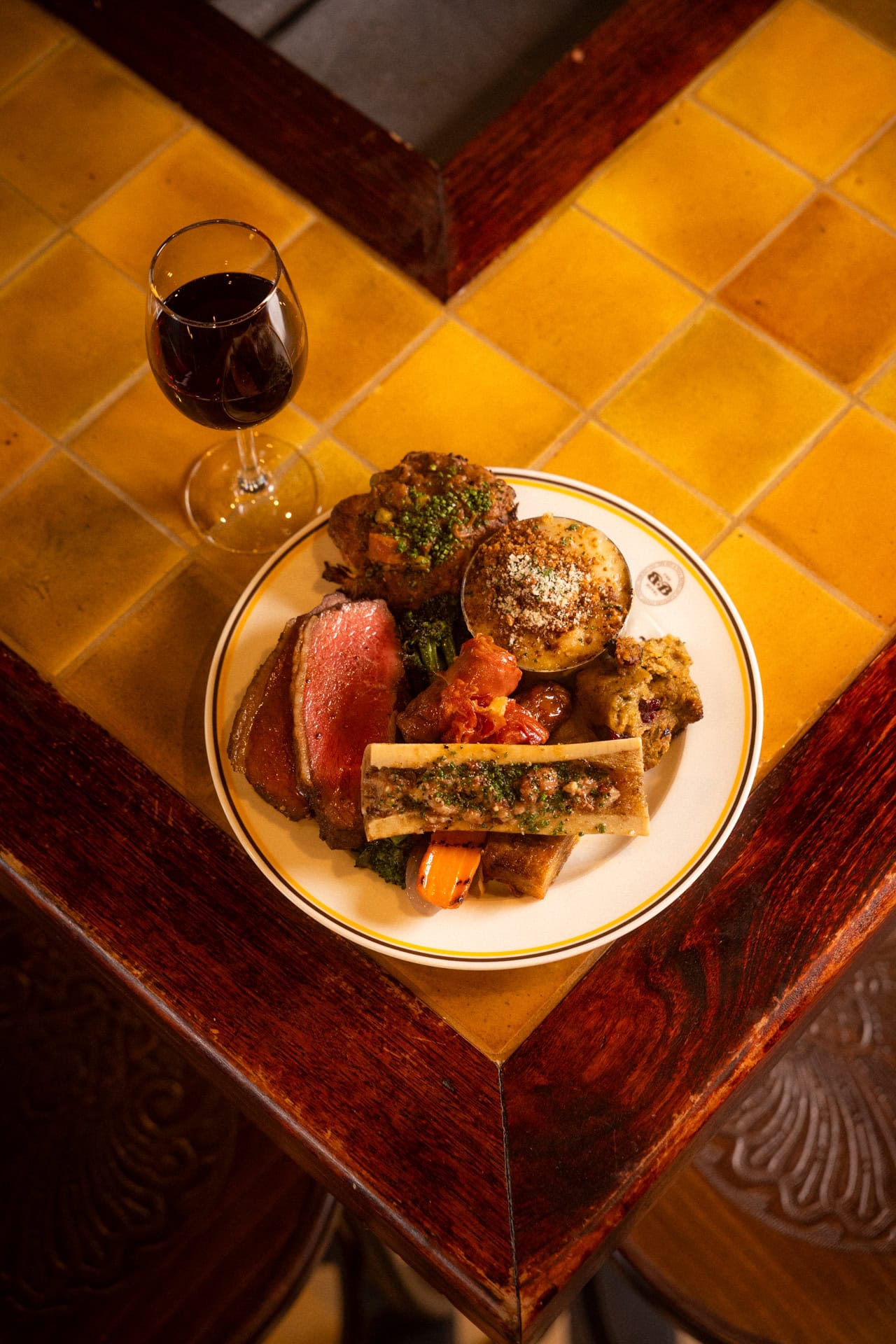 Sunday roast beef with bone marrow cauliflower cheese stuffing and glass of red wine on tiled table at The Bat and Ball Hotel Redfern Sydney