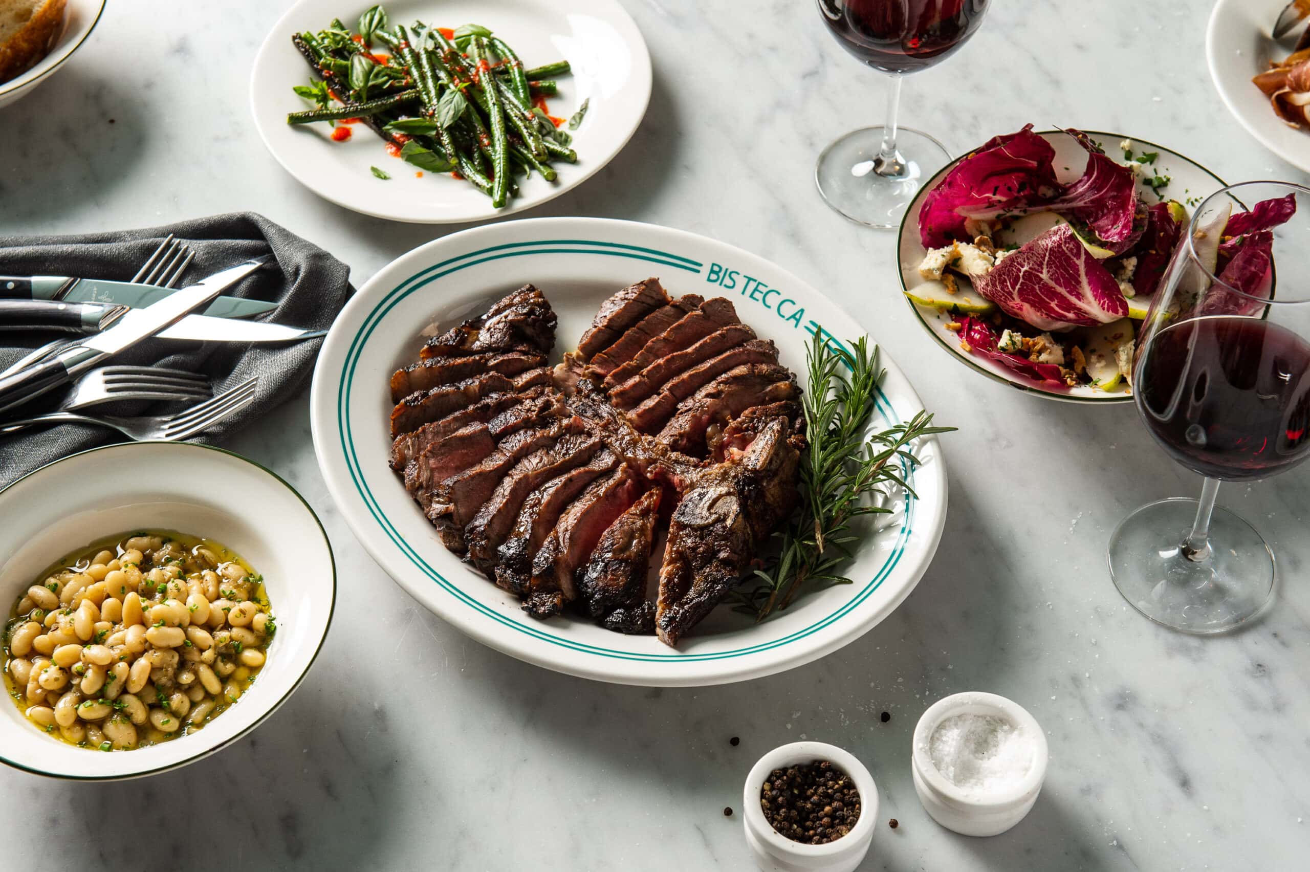 Credit: [photographer])Sliced T-bone steak with sides and wine at Bistecca Sydney