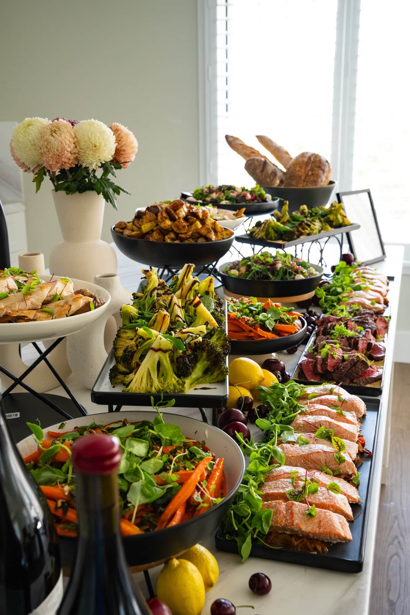 A tiered buffet spread featuring salmon, sliced beef, roasted broccoli, salads and sourdough, styled on black serving dishes in a bright private dining space