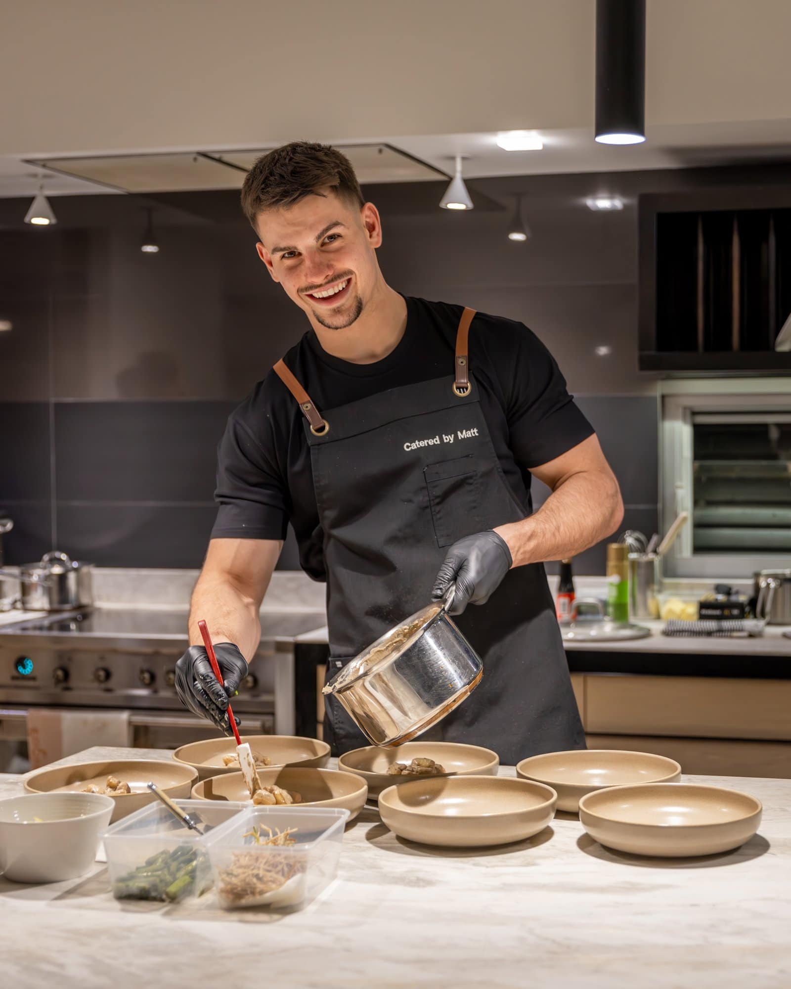 Chef Matt smiling while plating individual dishes at a kitchen bench during a private catering event