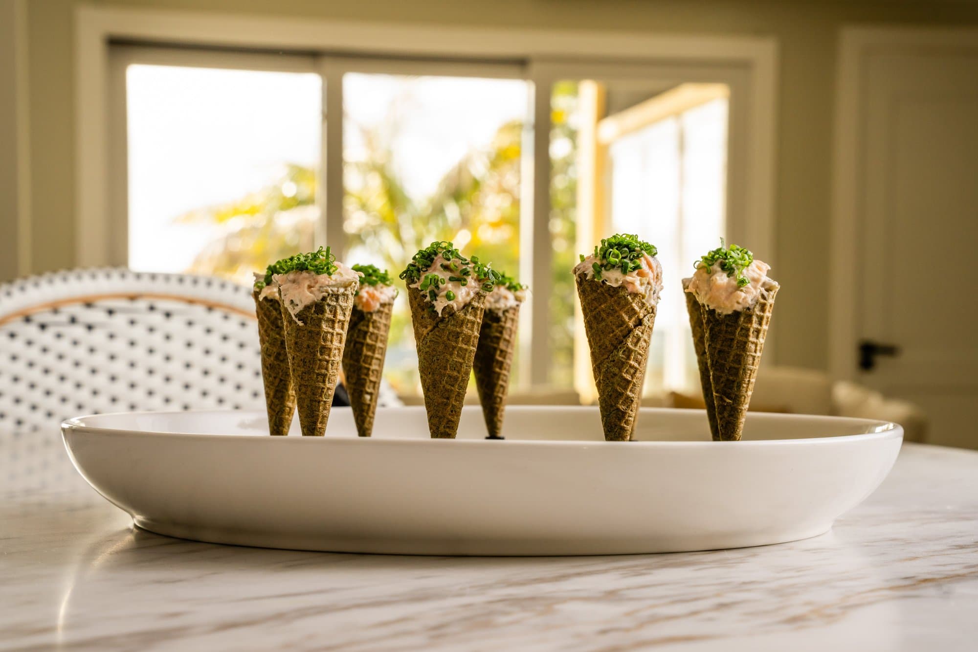 Smoked salmon rillette served in miniature seaweed waffle cones, presented upright in a white oval dish on a marble surface