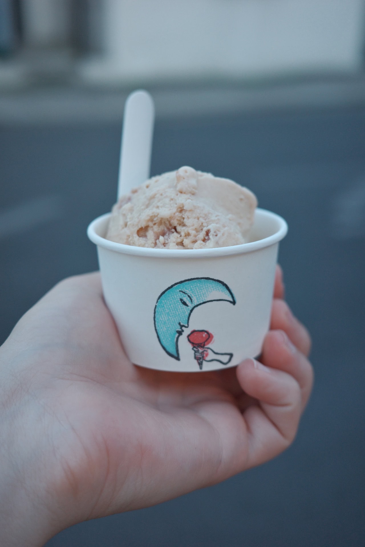Someone holding a scoop of ice cream in a tub, decorated with an illustration of a crescent moon, from The Dreamery in Islington.
