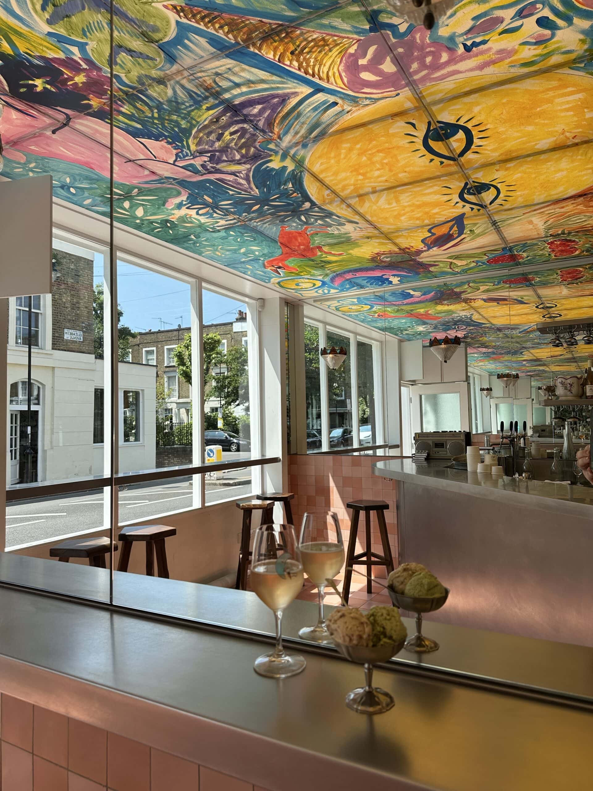 The handpainted, colourful ceiling of The Dreamery in London, featuring two glasses of wine and two silver bowls of ice cream.