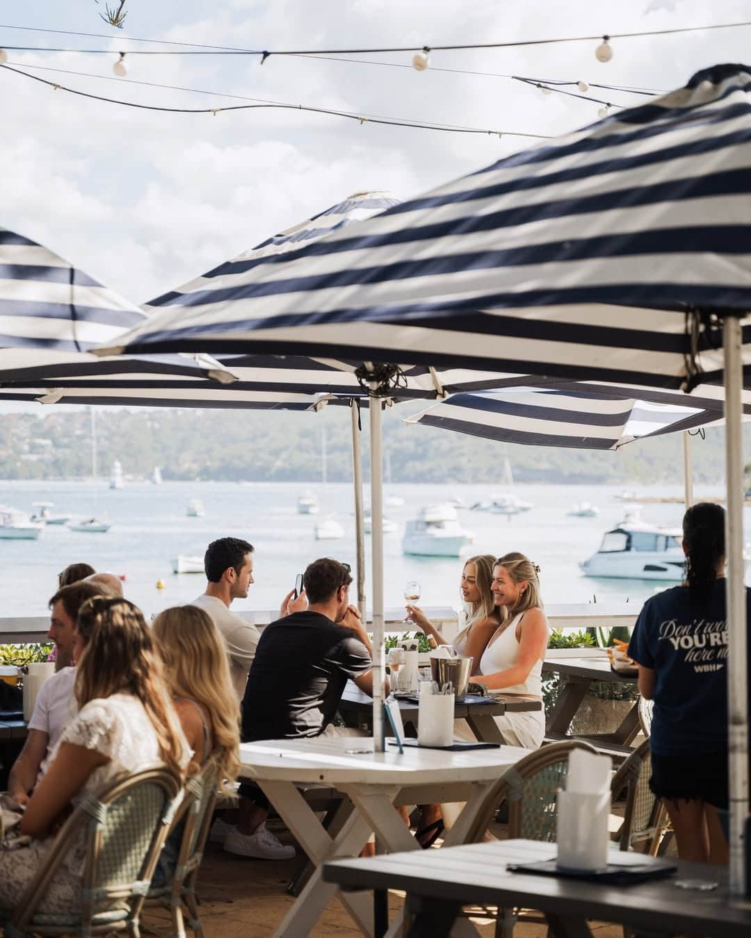 People enjoying the alfresco dining area and iconic blue and white striped umbrellas at Wastons Bay Hotel.