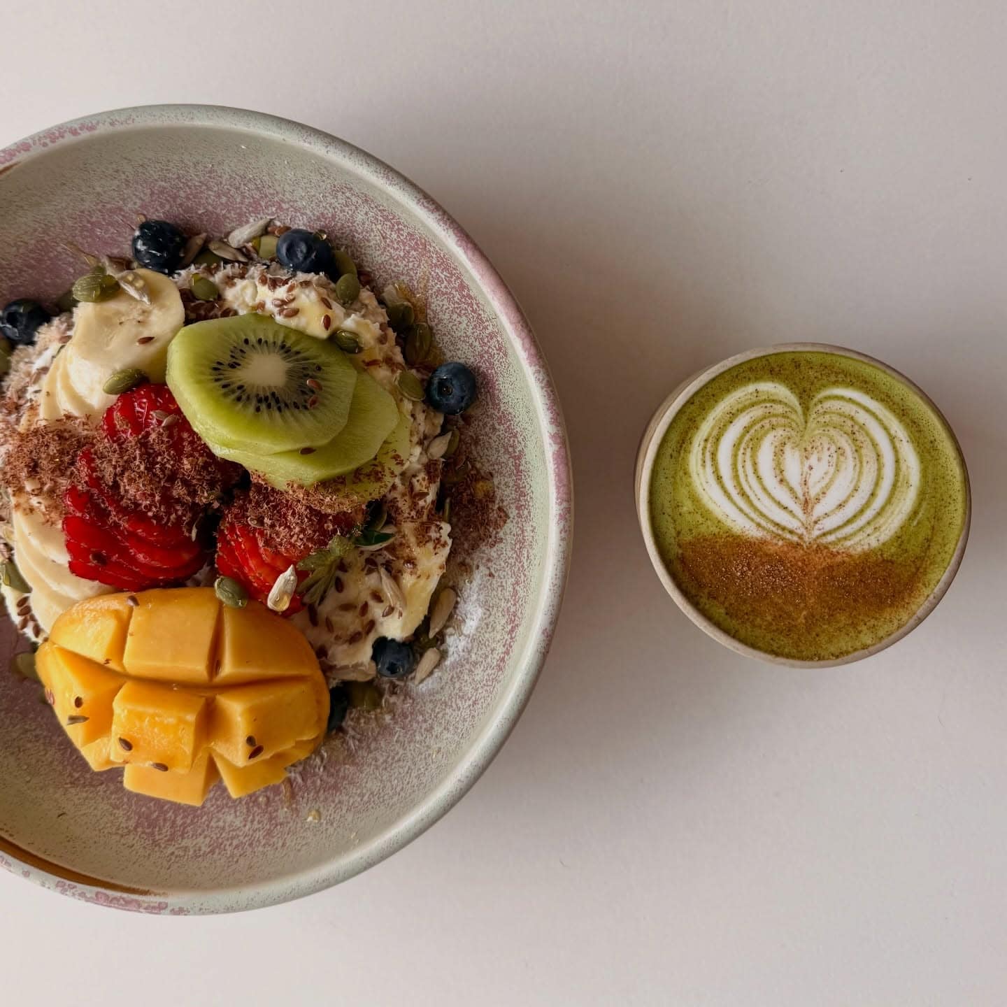 A bowl of bircher museli topped with colourful fruits next to a matcha latte at Coop in Bronte.