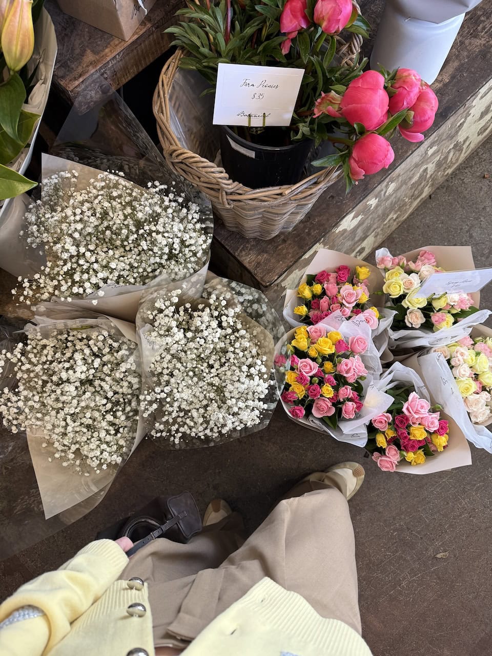 Overhead view of wrapped bunches of gypsophila, mixed roses, and farm peonies displayed outside Botanical Florist.