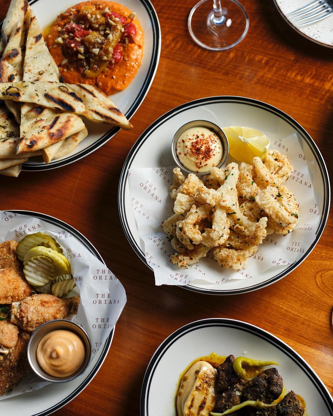 A top down view of a series of plates of food, including crispy calamari, at The Oriana in The Rocks.