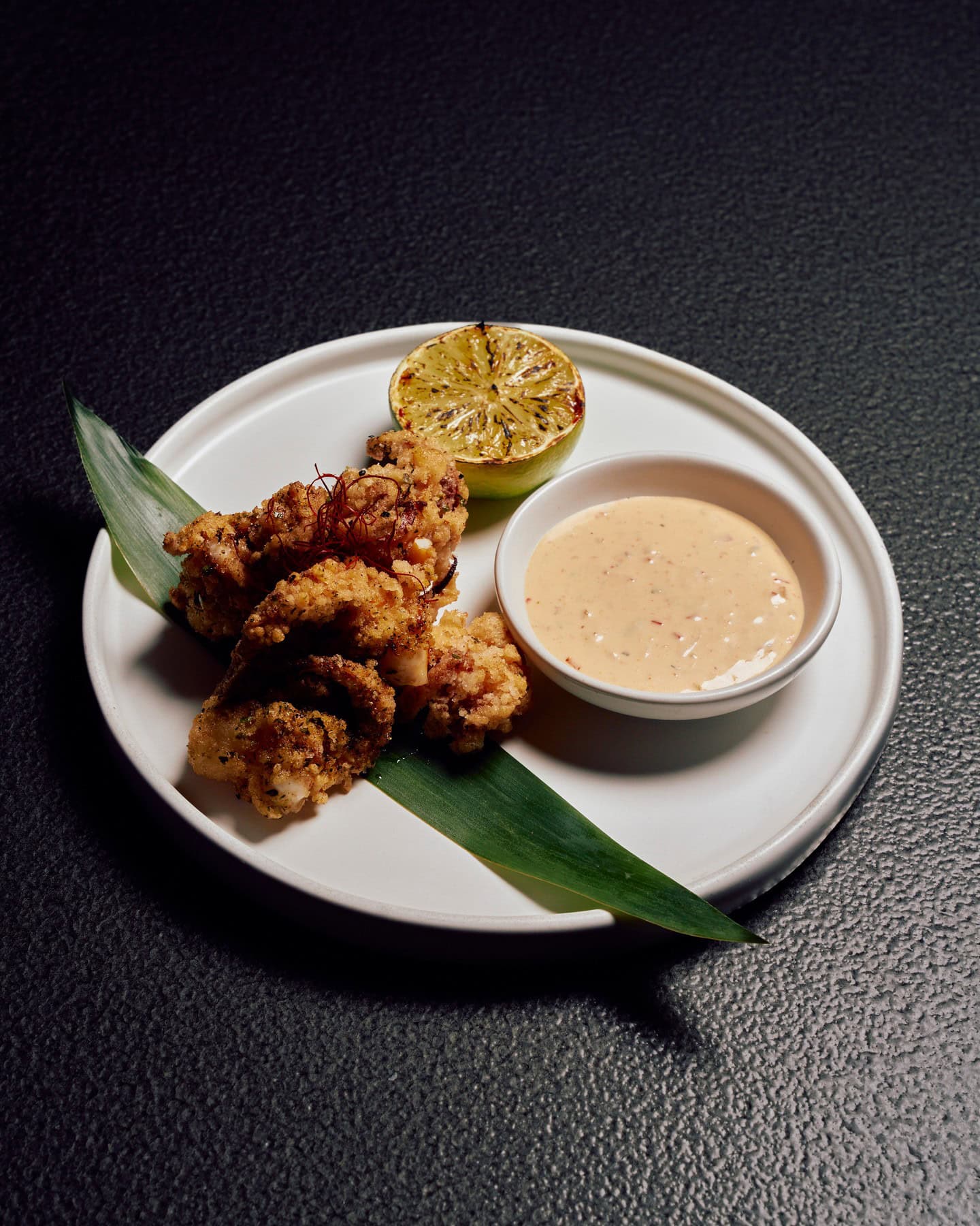 Fried chicken, sauce and a grilled lemon atop a plate decorated with a portion of palm leaf at honto in Brisbane.