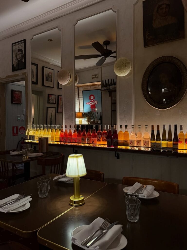 Moody dining room with backlit natural wine bottle display table lamps and eclectic wall art at Circa Espresso Parramatta Sydney