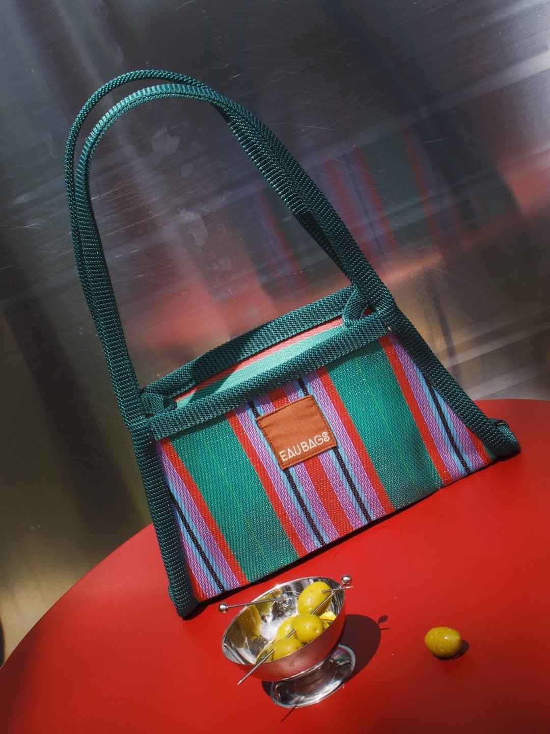 EAU BAGS multicolour striped mini handbag with green rope handles on red table with bowl of olives
