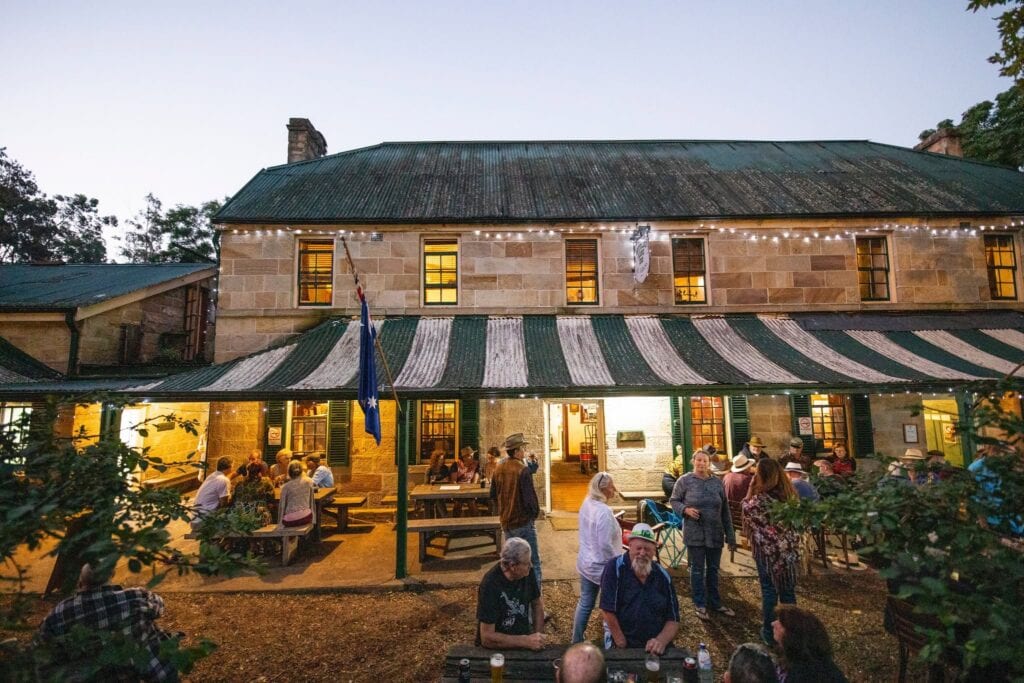 Sandstone exterior with diners in courtyard at dusk at Settlers Arms Inn St Albans NSW