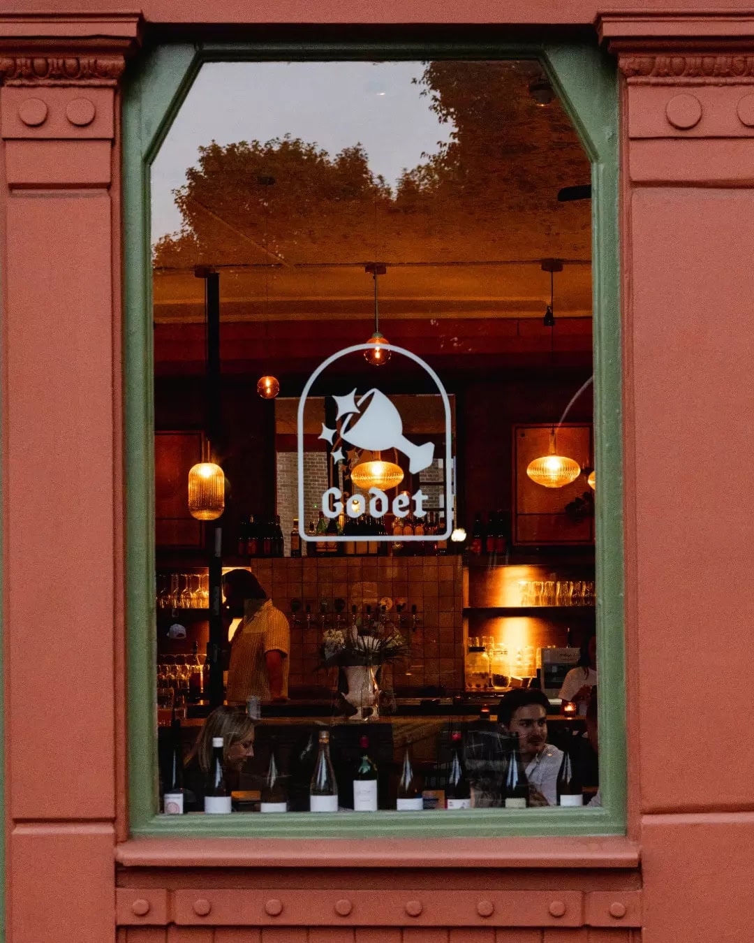 A green-framed window looking into the cosy wine bar Godet in Islington.