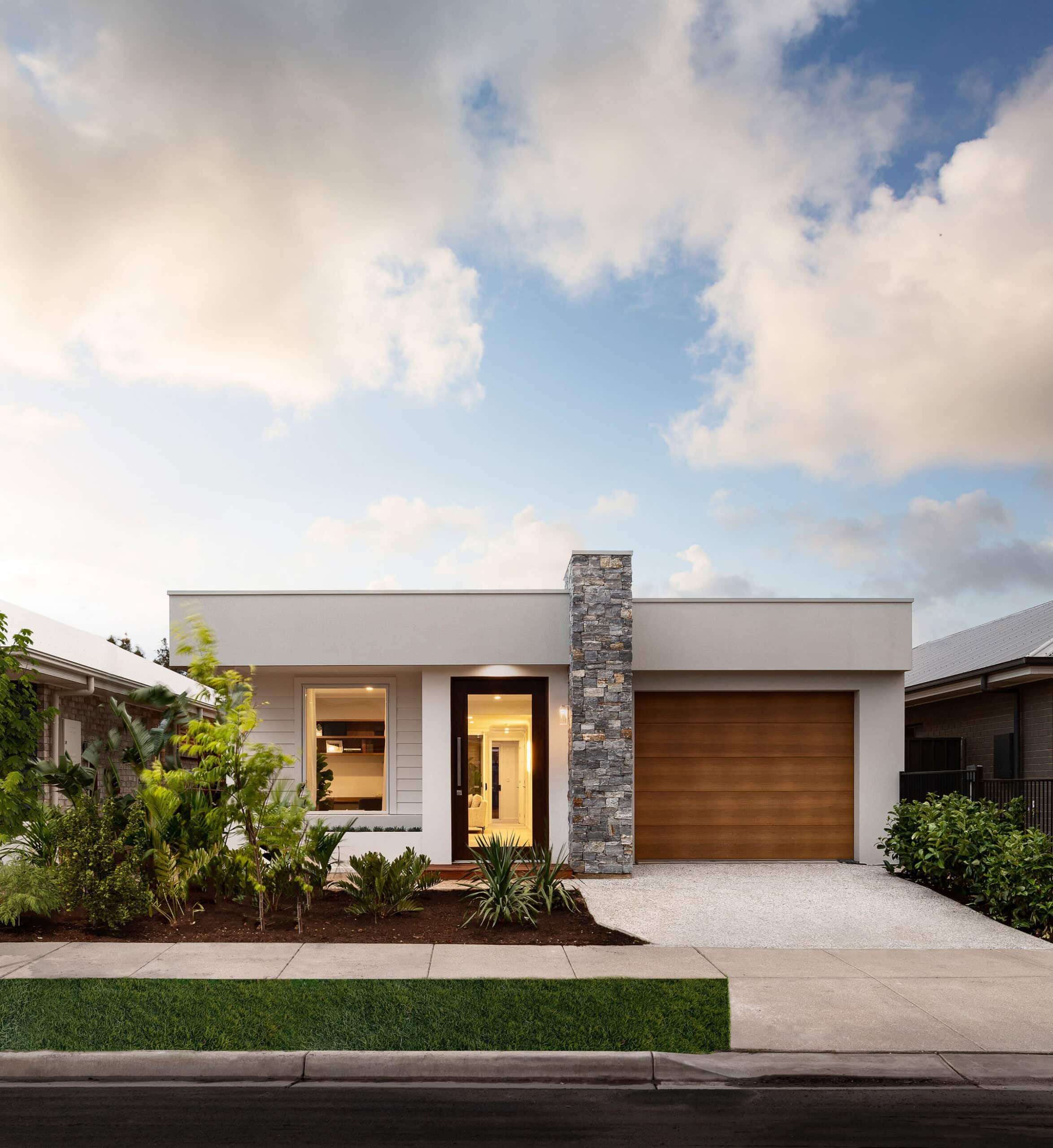 A modern display home by Weeks Homes at Playford Alive, featuring a rendered white facade, stone feature column, timber garage door and native garden landscaping.