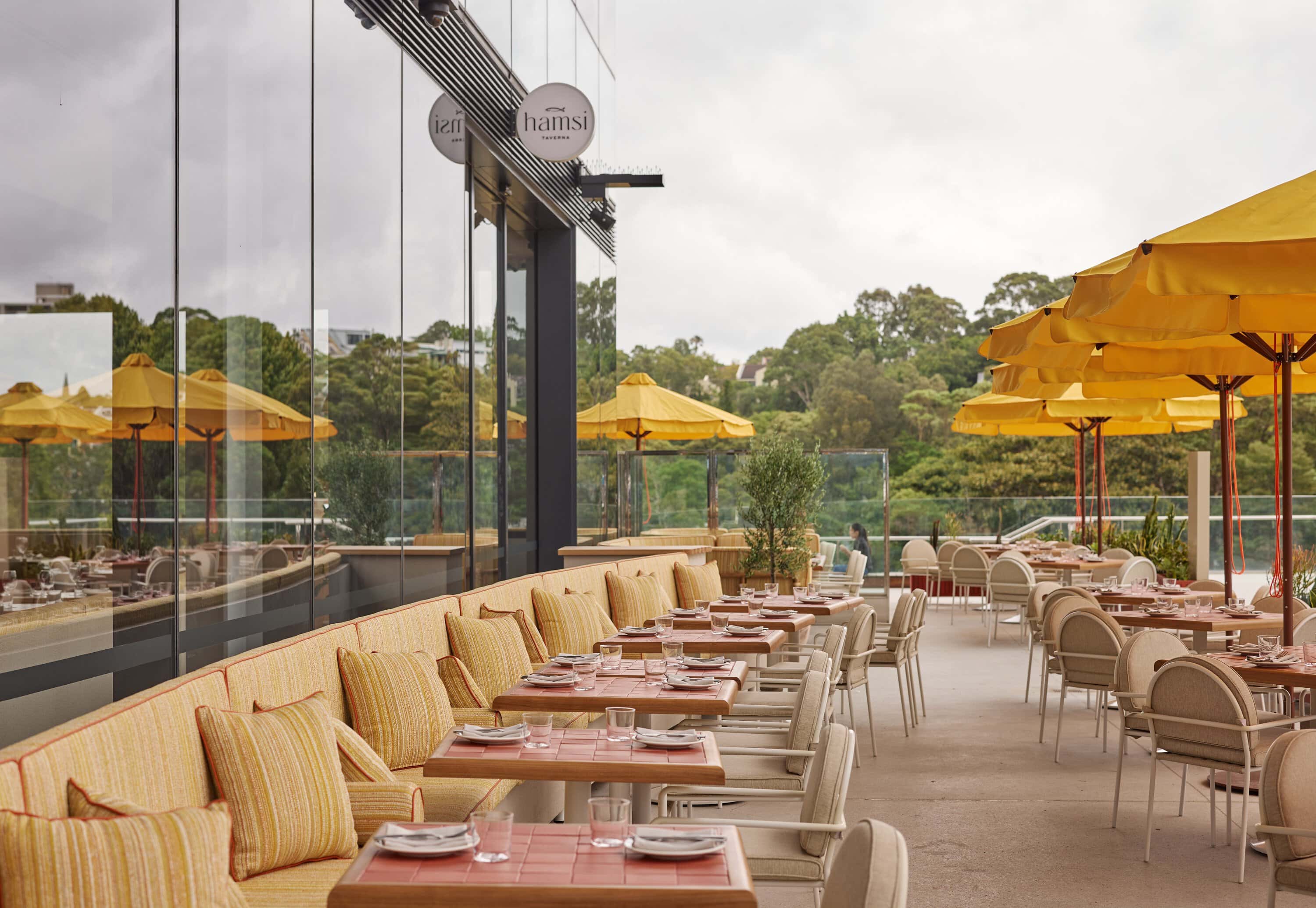 Hamsi Taverna outdoor terrace with yellow striped banquette seating tiled tables and yellow umbrellas overlooking greenery Sydney Fish Market Pyrmont