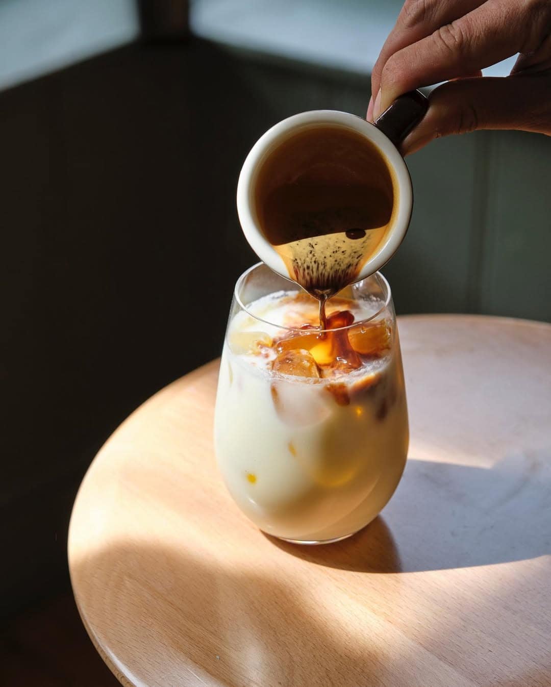 Someone pouring a coffee shot into a glass of icey mik at high ground in islington.