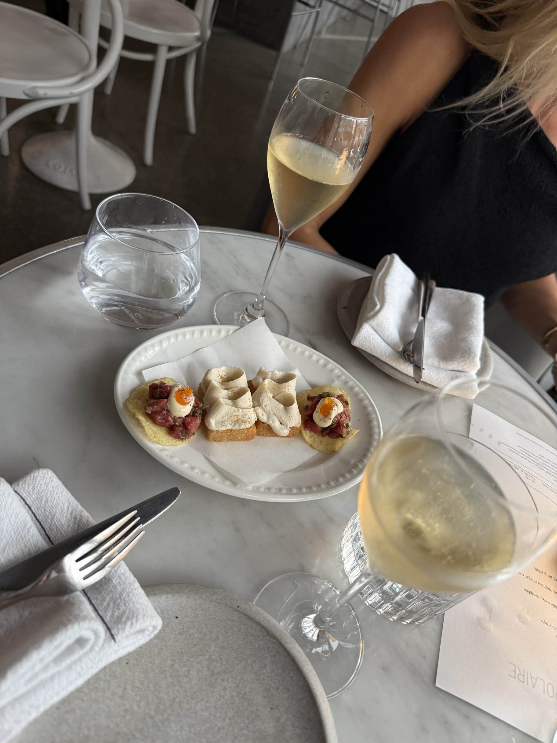 Beef tartare toasts and two glasses of white wine on a marble table at Ins Polaire.