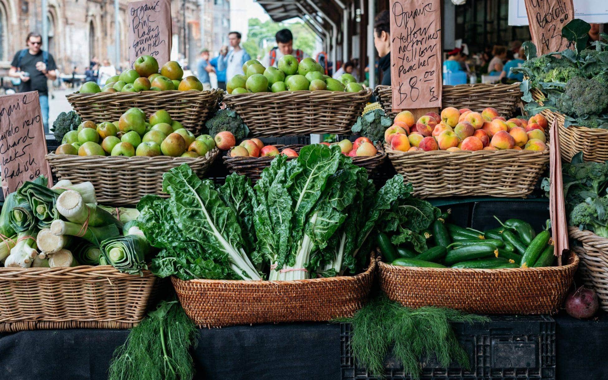 Organic fruit and vegetable stall with wicker baskets apples silverbeet and cucumbers Carriageworks Farmers Market Eveleigh Sydney