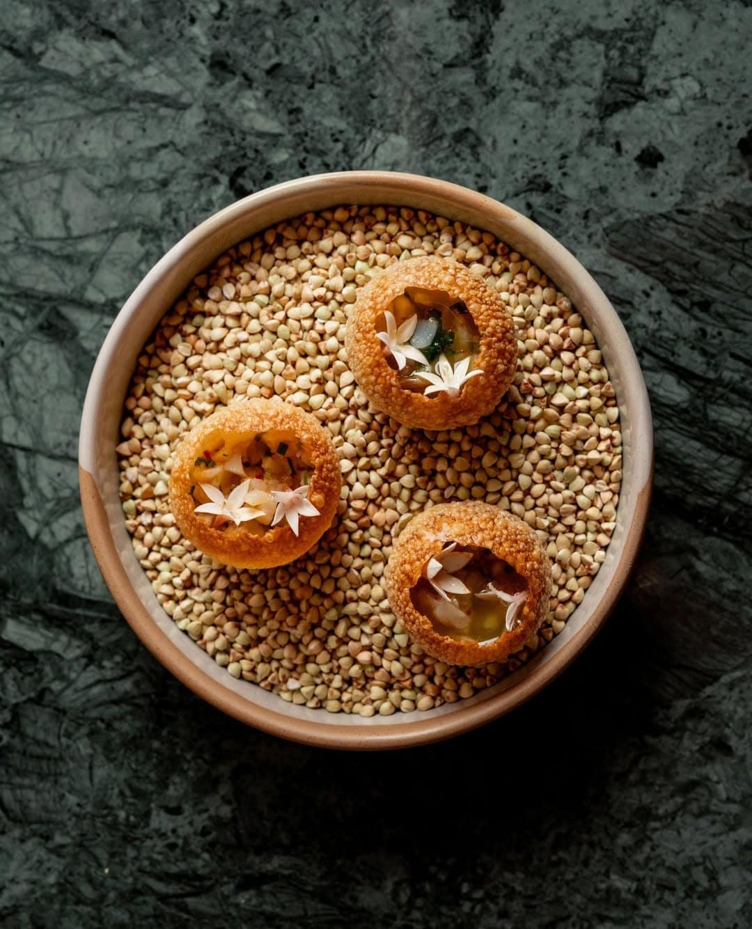 A plate of three pani puri atop grains in a bowl at Layla in Brisbane.