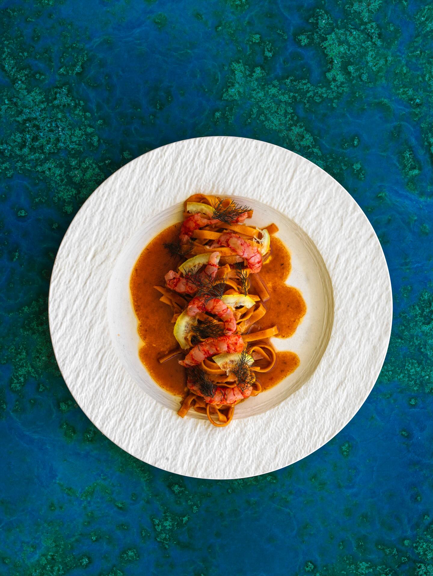 A plate of prawn pasta atop an aqua table at icebergs in bondi.