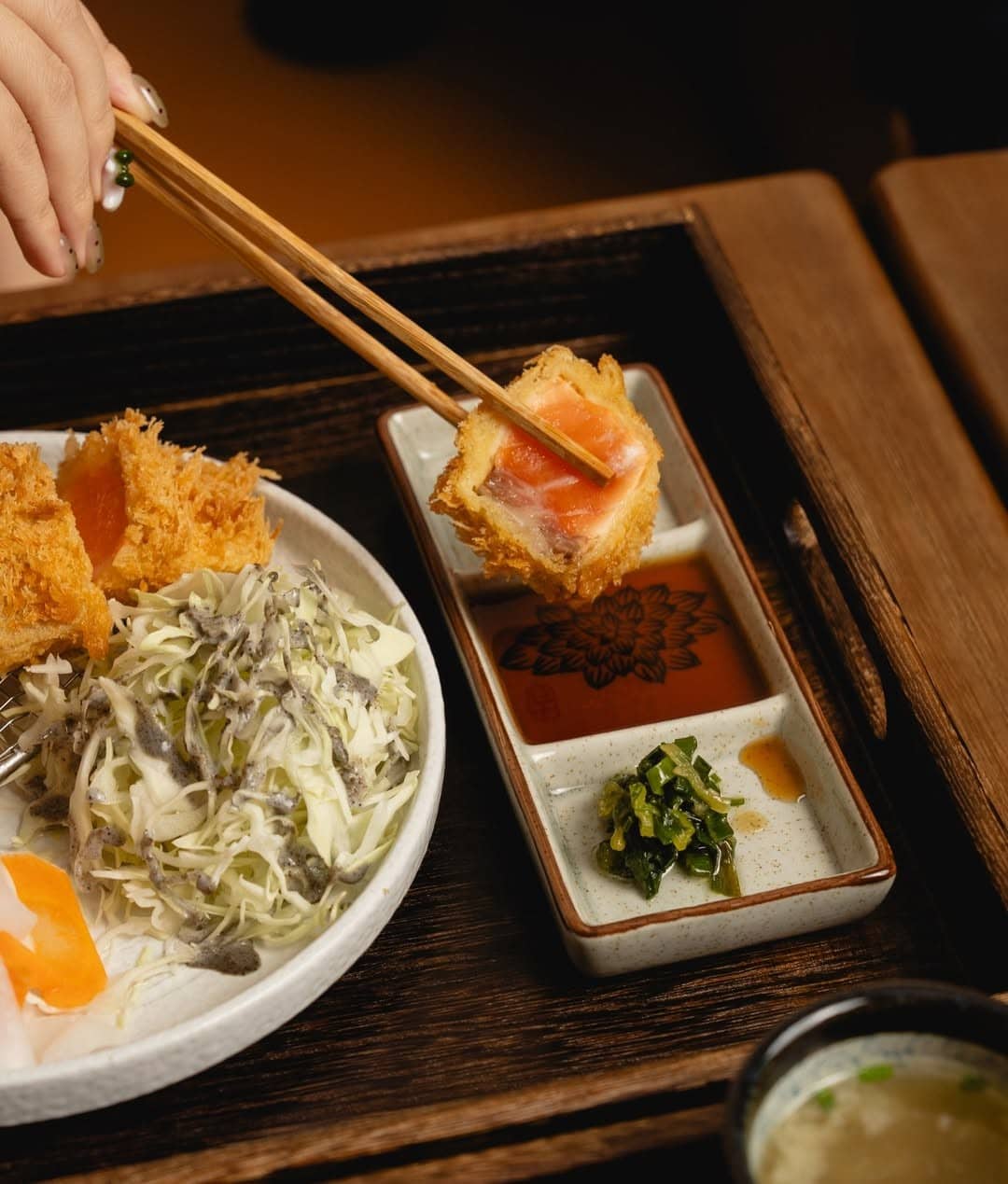 Senkatsu wagyu gyukatsu held with chopsticks over dipping sauce with shredded cabbage salad Sydney CBD