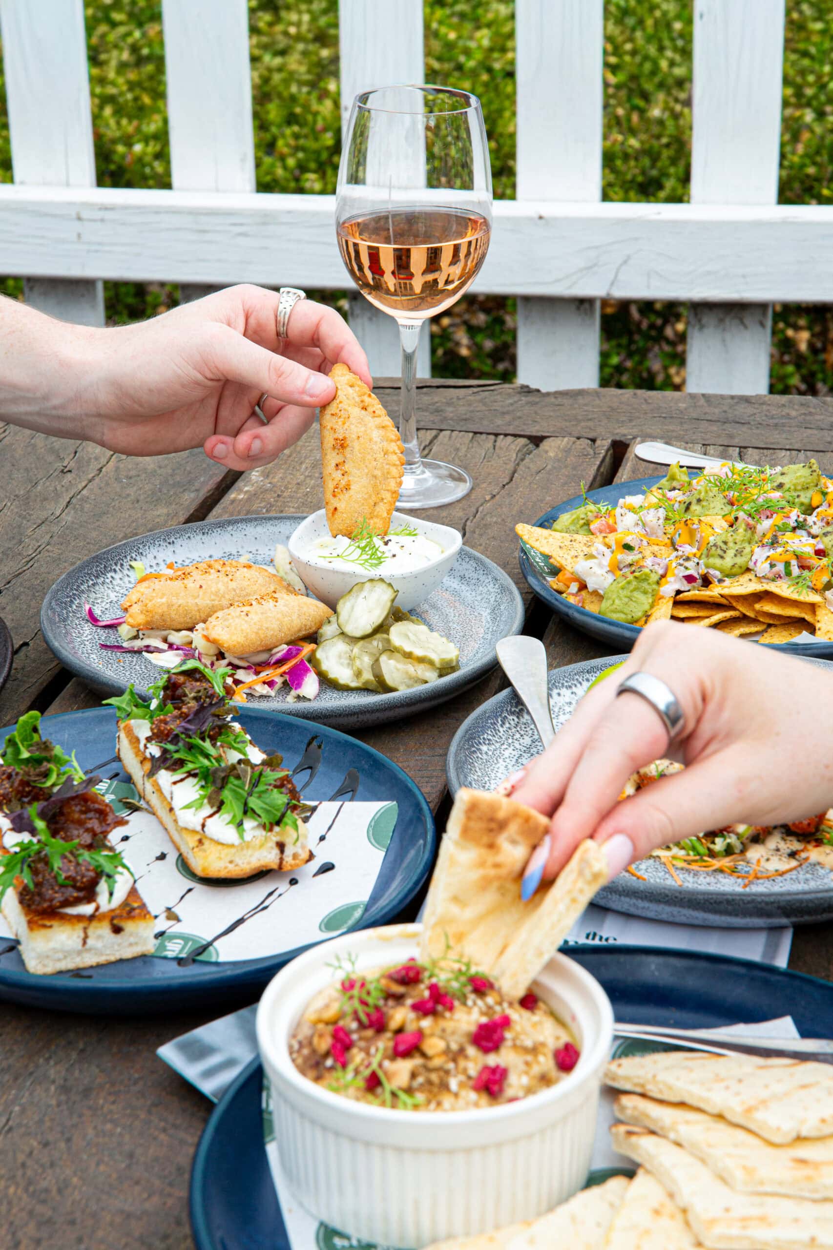 Shared plates including dips flatbread nachos and toast with rose wine on outdoor table The Greens North Sydney