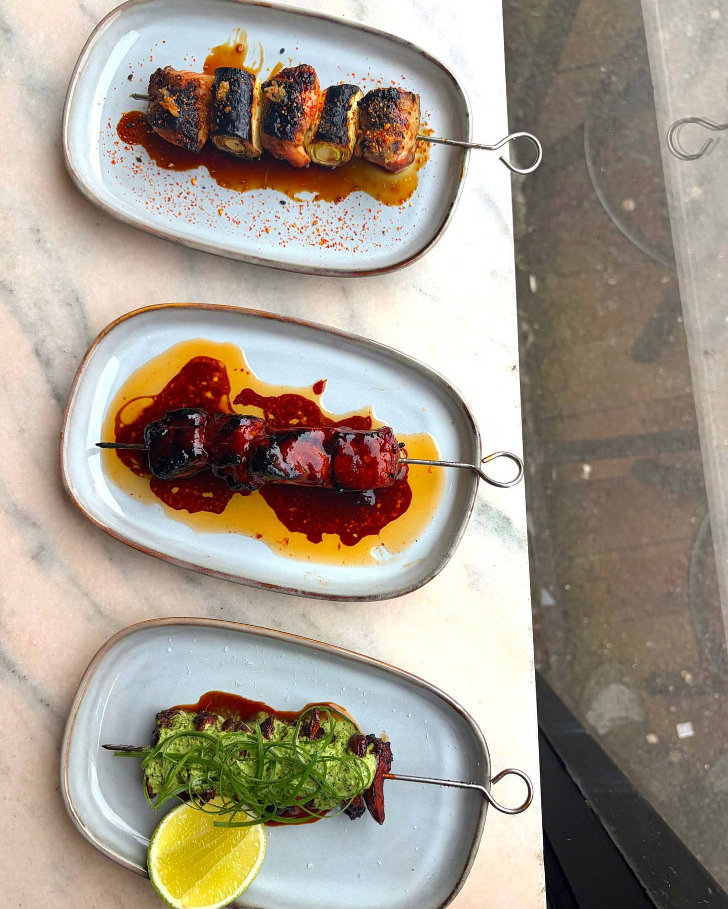 Three seperate skewers and matching sauces, sitting on seperate plates, at top cuvee in highbury.